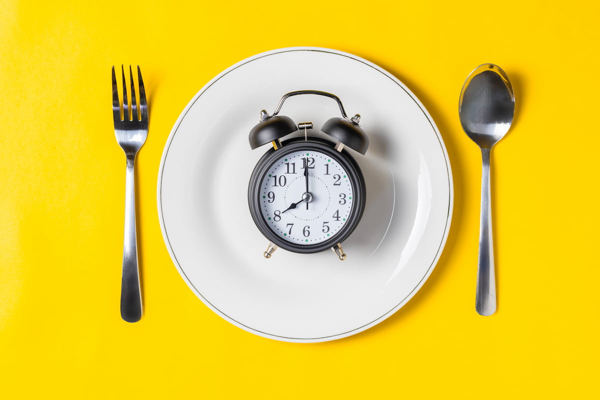 A plate with a clock on top of it, with a spoon and fork beside it