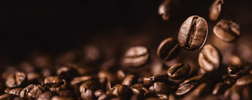Coffee beans are falling and landing among other beans, creating a dynamic, scattered effect against a dark background.