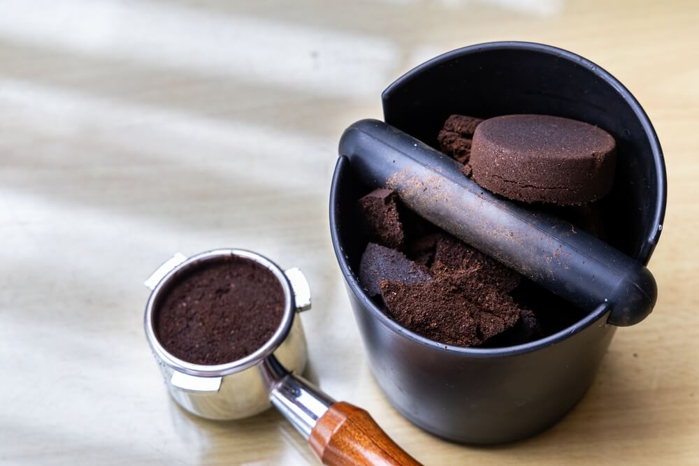 Fresh Mystic Monk coffee grounds in a portafilter with a knock box next to it.