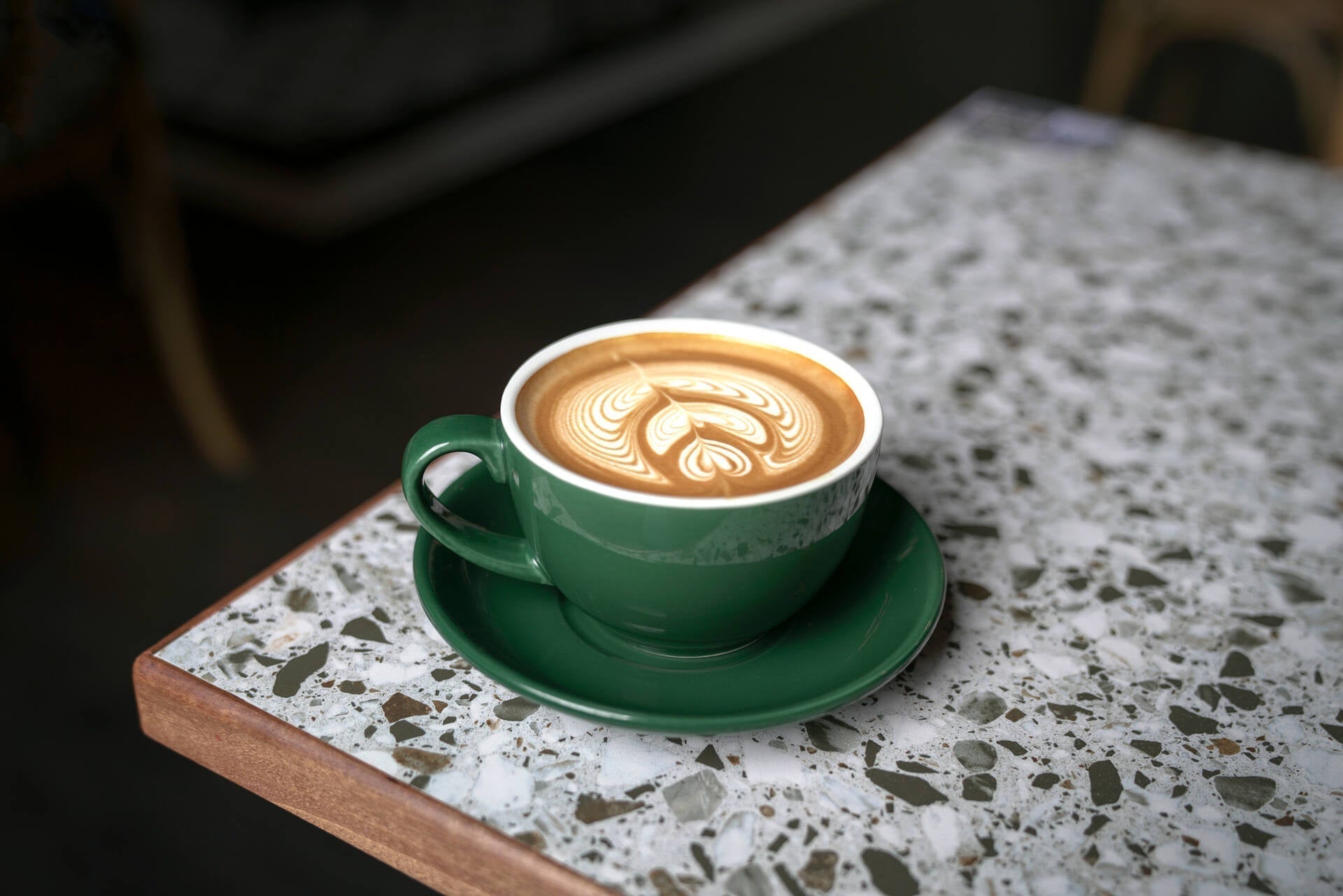 A green mug with a cup of flat white coffee topped with white foam milk resting on a table