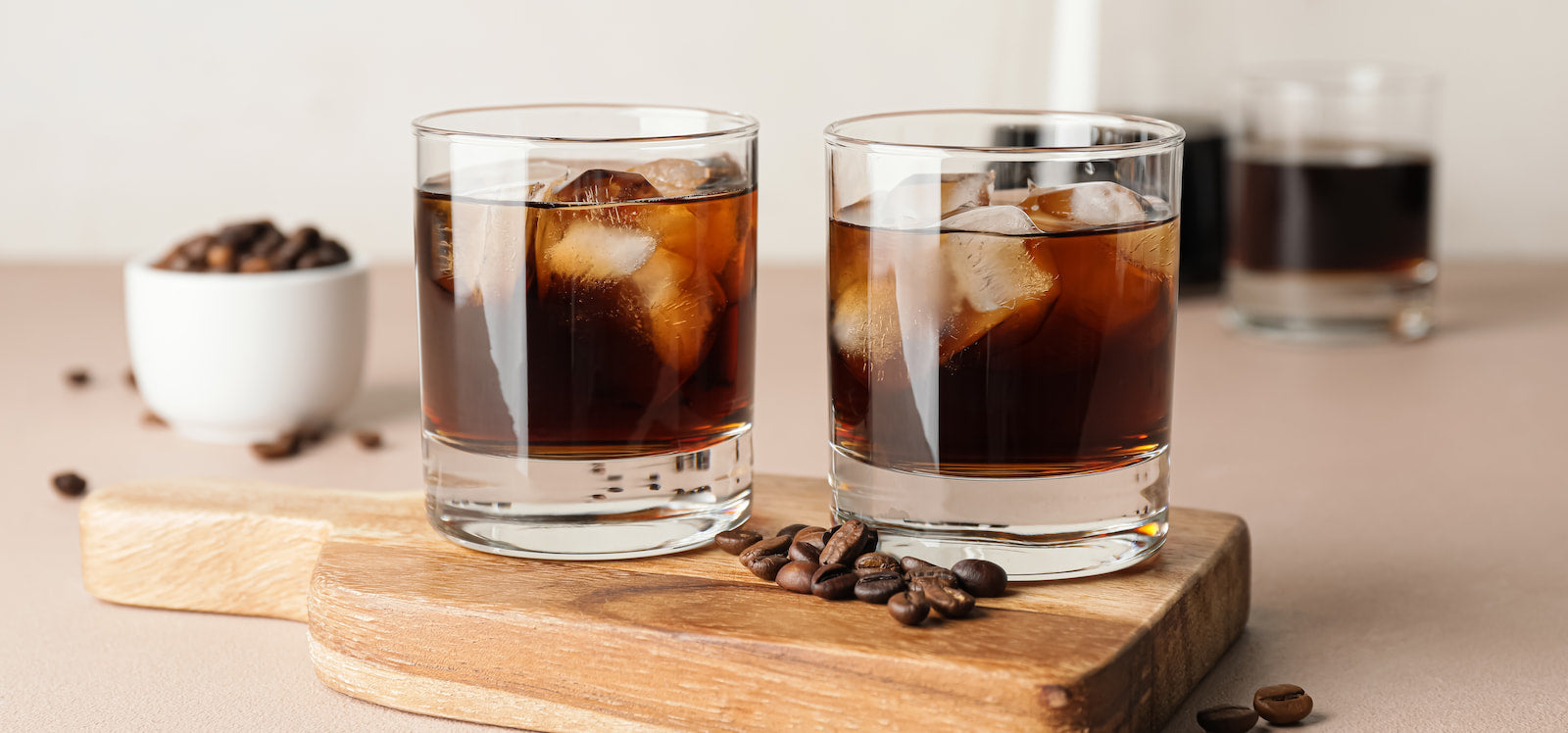 Two glasses of cold brew over ice on a paddle-sized cutting board with fresh coffee beans sitting on top