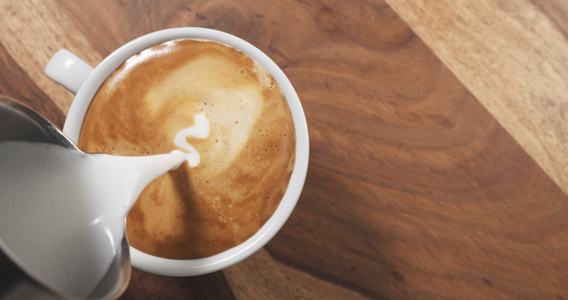 Someone pouring half and half into a mug to make a breve coffee