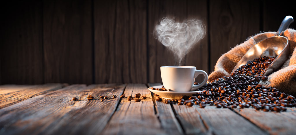 A white coffee cup with heart-shaped steam on rustic wood near an open bag of coffee beans