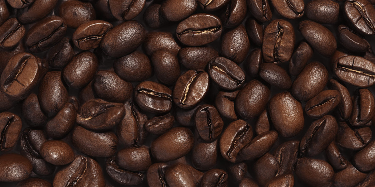 Glossy coffee beans are scattered closely together, highlighting their rich brown color and smooth texture. The image focuses on the intricate details of the beans' surfaces in a tightly packed arrangement.