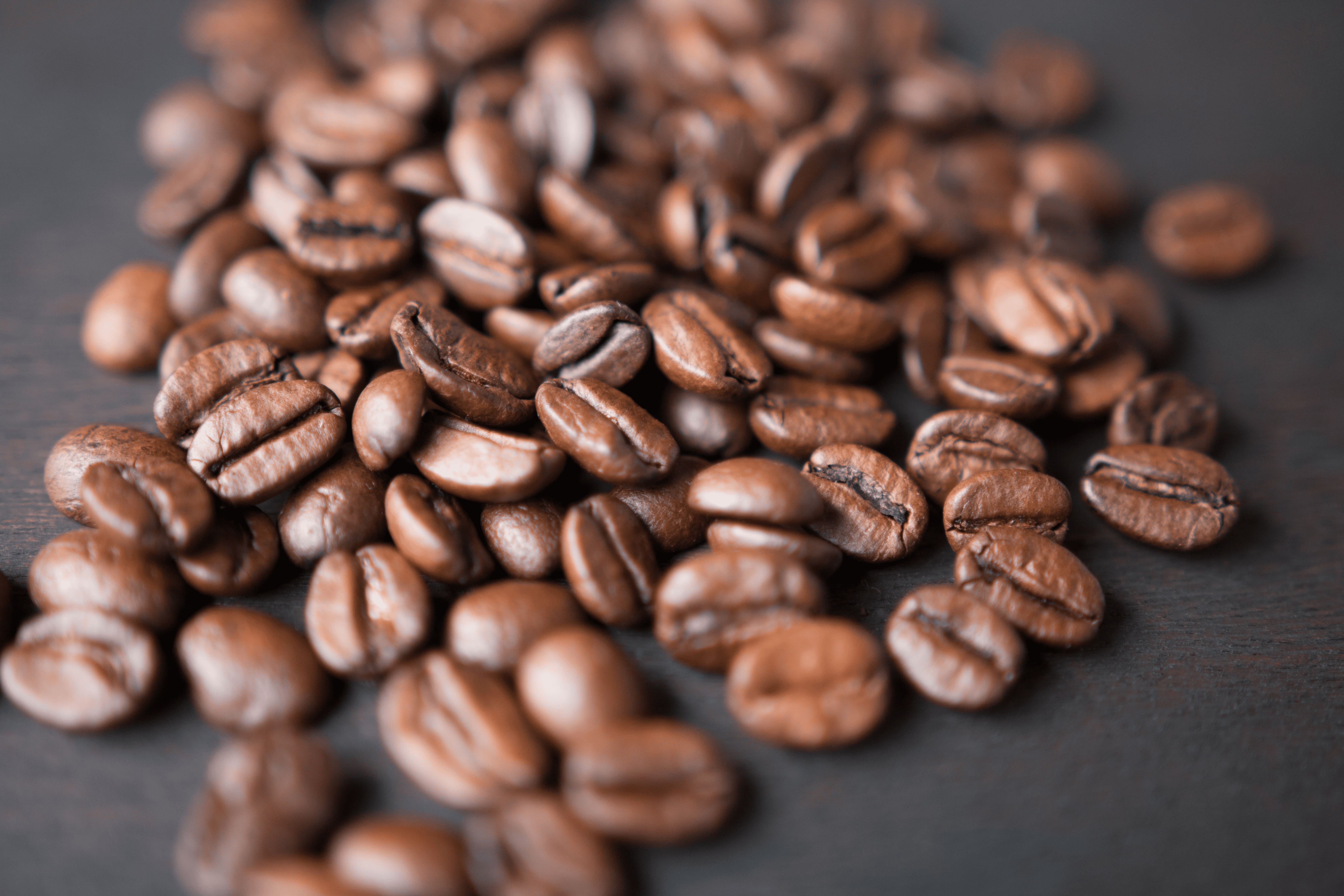 Coffee beans lie scattered across a dark wooden surface, showcasing their glossy, rich brown texture, creating a sense of warmth and aroma.