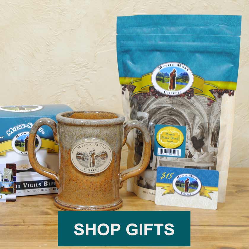 Double Handled mug with Mystic Monk Logo, a 12oz bag of coffee, a box of Monk-Shots, and a gift card arranged on a table. Text reading Shop Gifts.