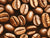 Brown coffee beans lying still, closely packed together, creating a textured surface. The light reflects softly, highlighting their smooth and slightly shiny surface within a rich, dark background.