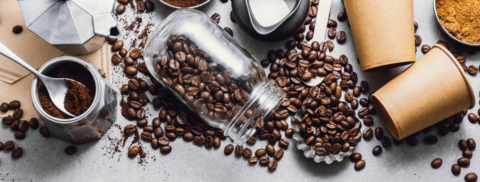 Flatlay of coffee beans spilling out of a jar, surrounded by coffee cups and coffee pots