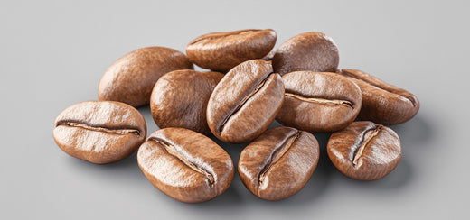 Coffee beans are scattered and resting on a smooth, light gray surface. The beans are shiny, with visible natural grooves and variations in texture.