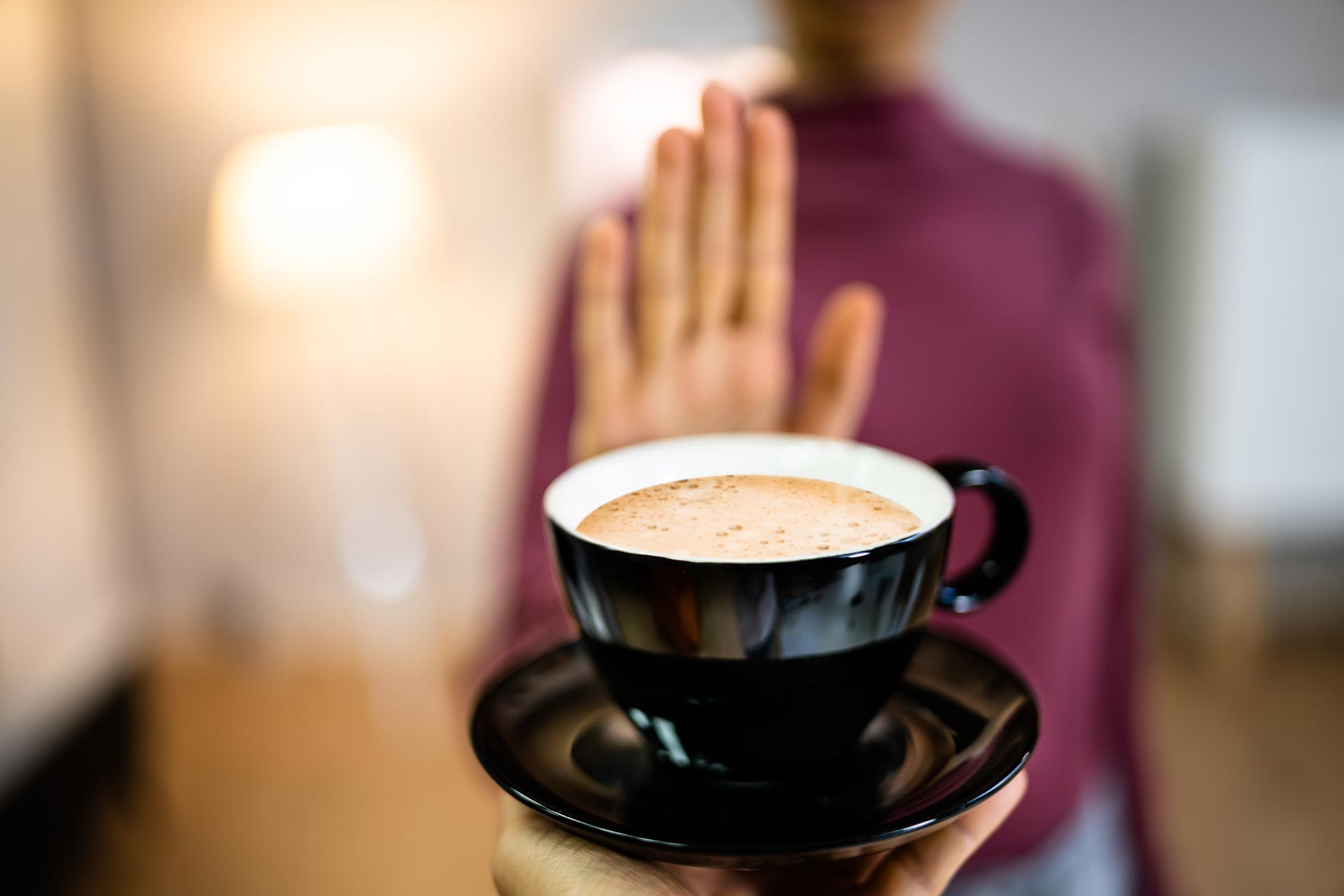 A person raising a hand to decline a cup of coffee due to acid reflux