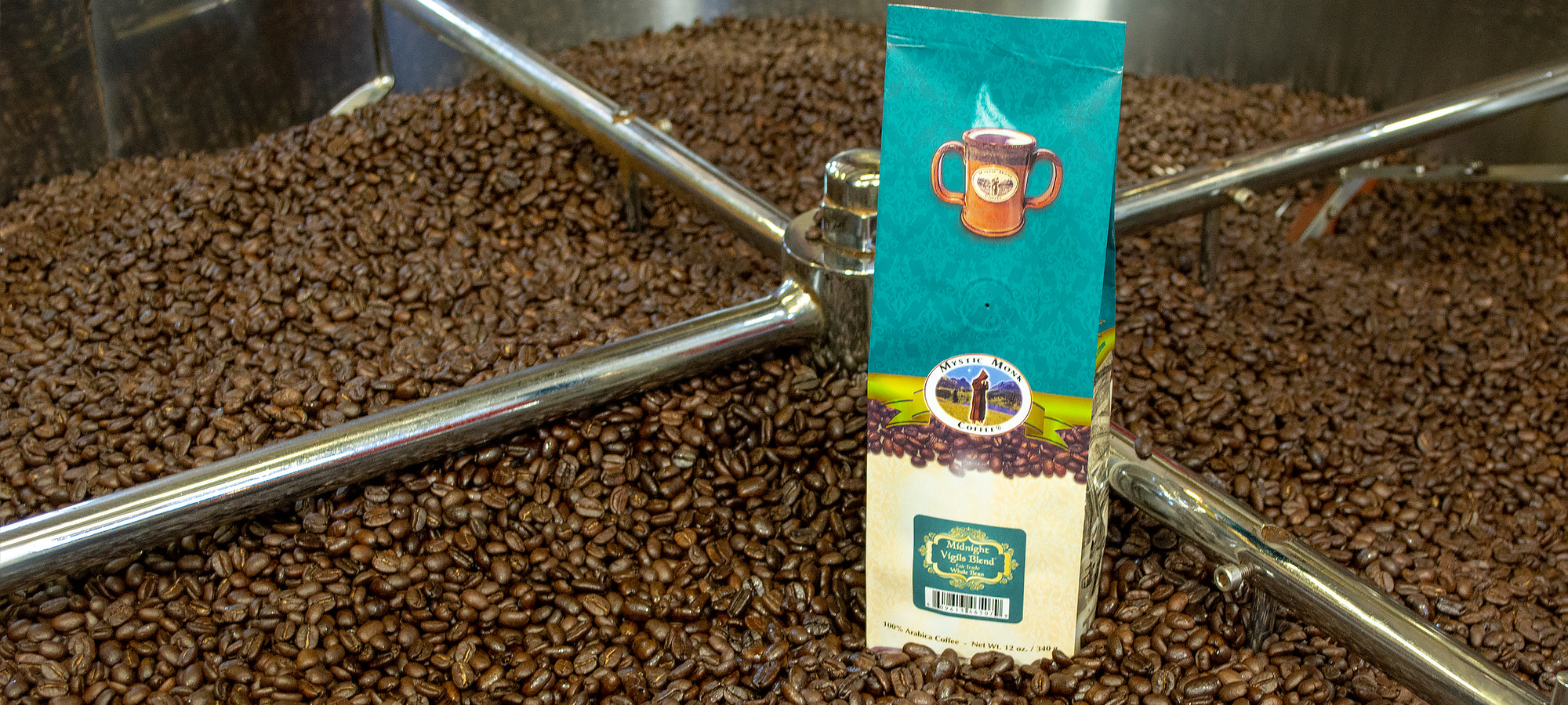 12oz bag of Mystic Monk Coffee sitting on a large amount of roasted coffee beans.