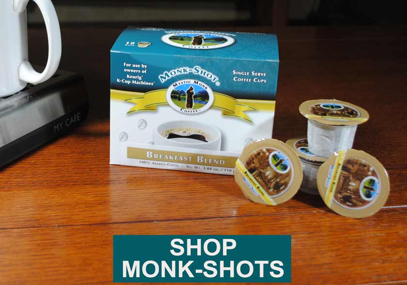 Text shop Monk-Shots with box of single serve Monk-Shots, with three individual K-Cup compatible Monk Shots in the foreground, all sitting on a brown wooden table.